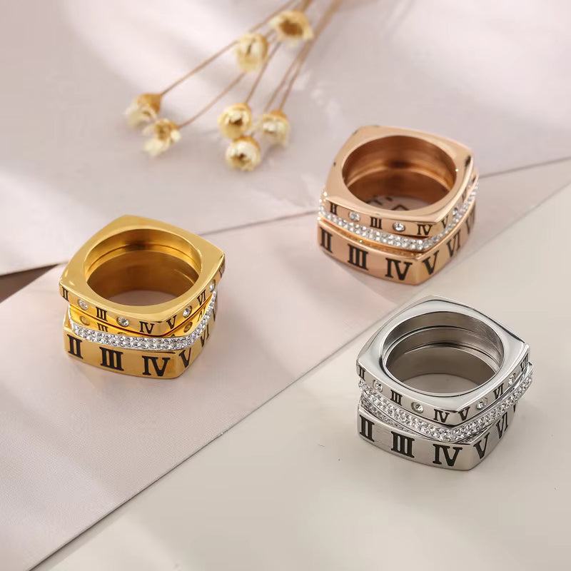 Three rings in gold, rose gold, and silver with Roman numeral design on a light background.