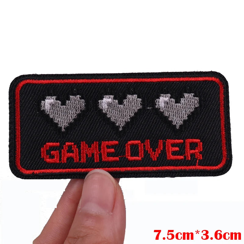 Embroidered patch with 'GAME OVER' text and pixelated hearts held by a hand, with dimensions displayed.