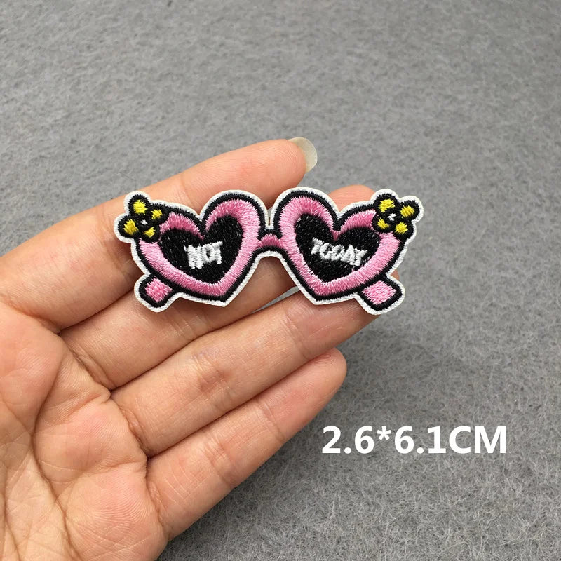 Heart-shaped sunglasses patch held in a hand with a gray background