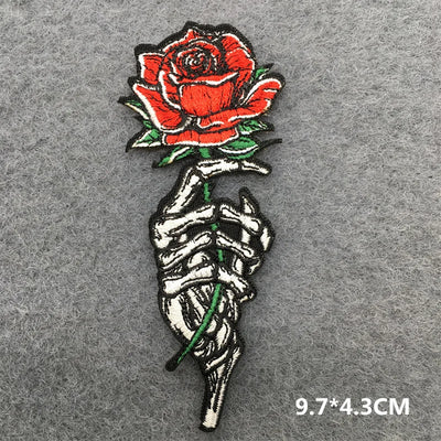 Embroidered patch of a skeleton hand holding a red rose on a gray background