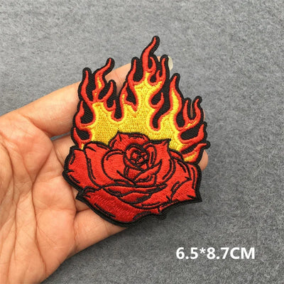 Flame-topped rose patch held by a hand on a gray background