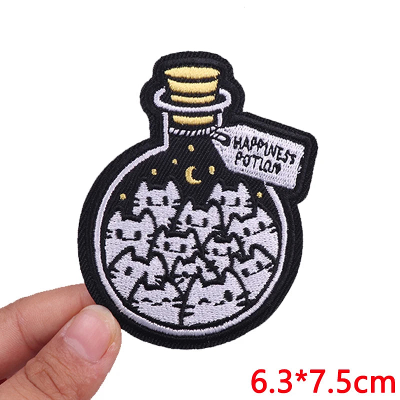 Embroidered patch of a potion bottle with cats and 'Happiness Potion' text, held by a hand.
