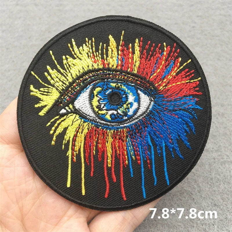 Colorful embroidered eye patch held by a hand on a gray background
