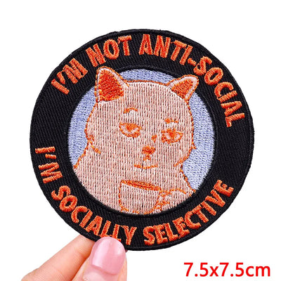 Circular patch with a cat illustration and text 'I'm not anti-social, I'm socially selective' held by a hand.