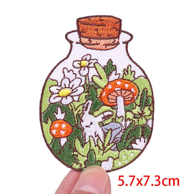 Embroidered patch of a bottle with nature scene including flowers, mushrooms, and a rabbit.