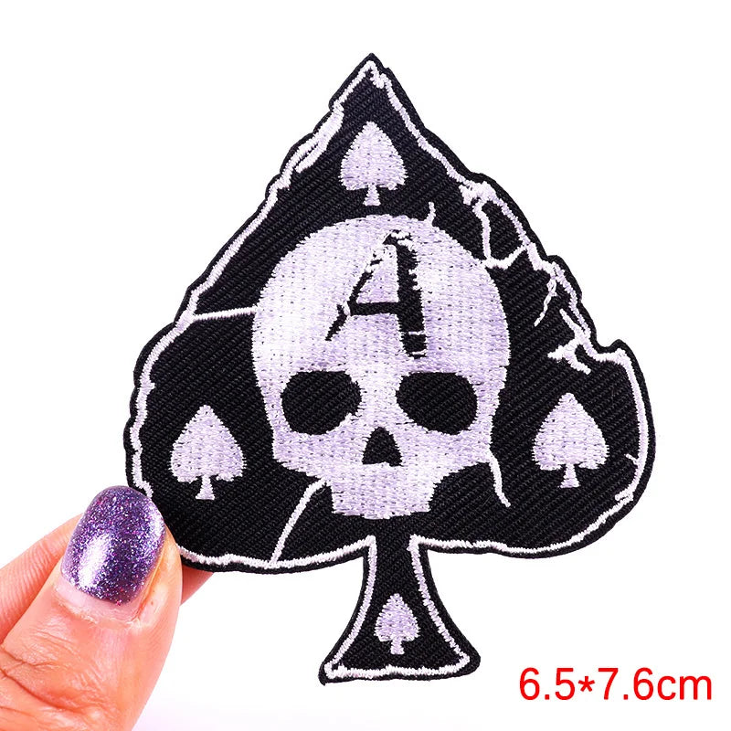Skull and spade design patch held by a hand with purple nail polish on a white background.