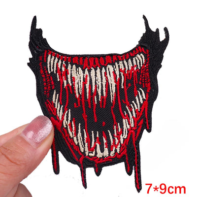 Decorative patch with red and black design held by a finger on a white background