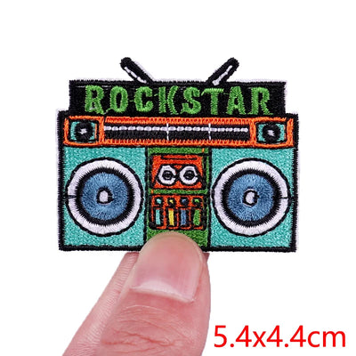 Embroidered patch of a boombox with 'ROCKSTAR' text held between fingers, size 5.4x4.4cm.