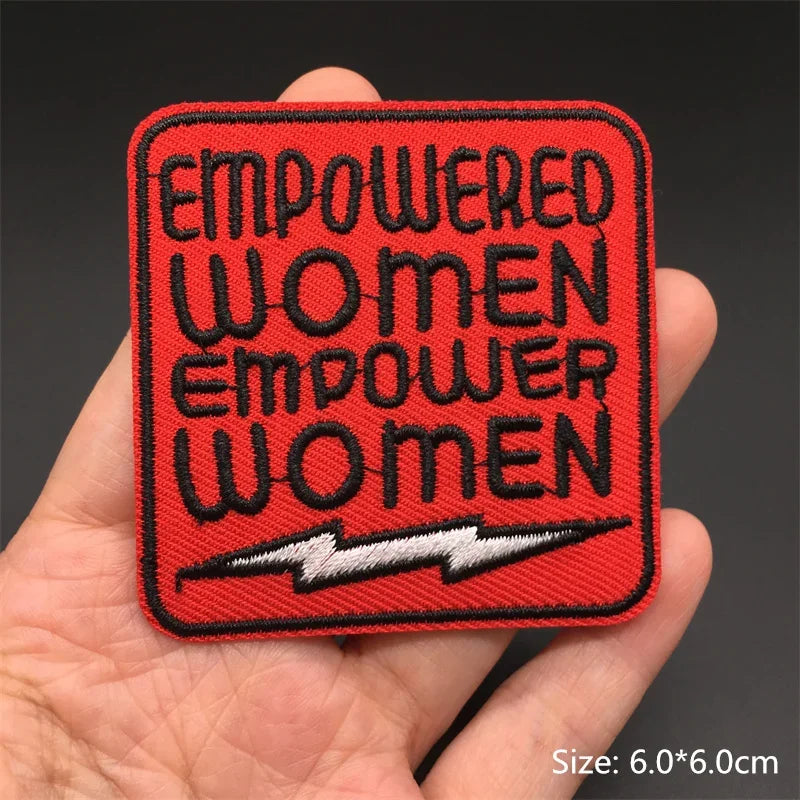 Red patch with 'Empowered Women Empower Women' text held in a hand against a dark background