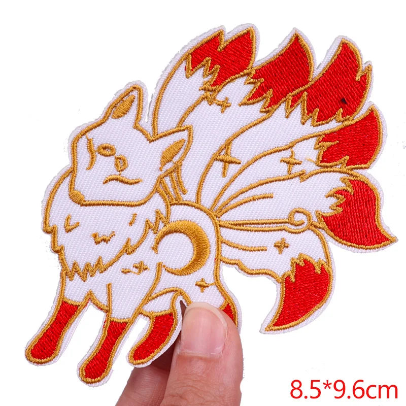 Embroidered patch of a fox with red and gold details held by a finger on a white background.