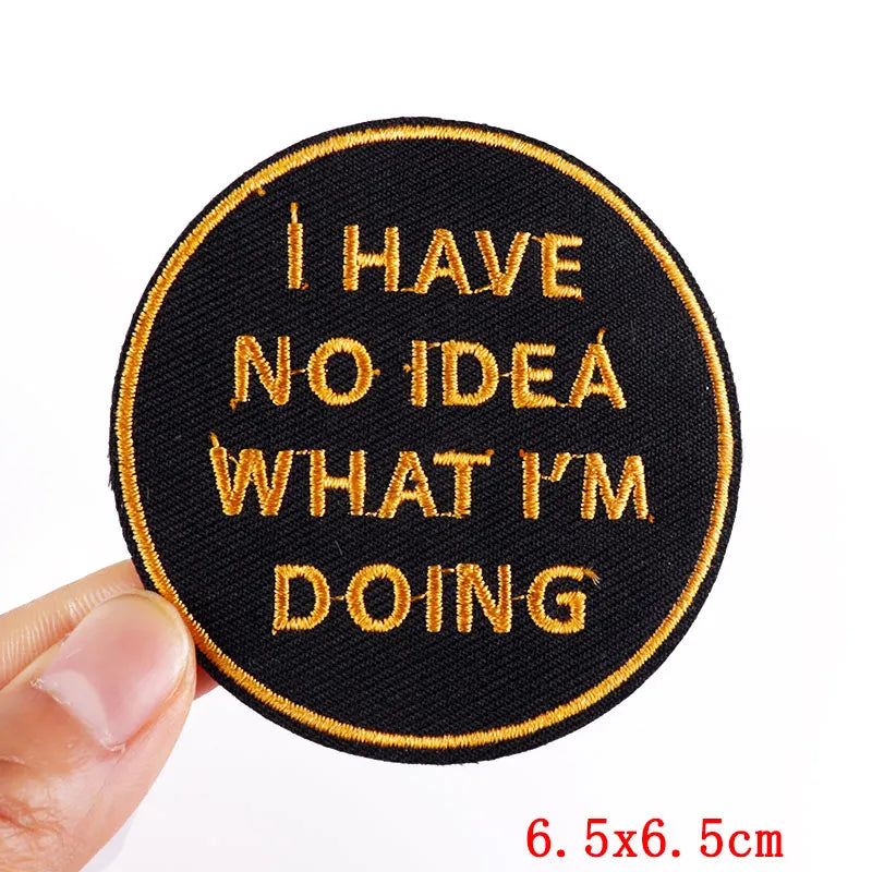 Round black patch with gold text 'I HAVE NO IDEA WHAT I'M DOING' held by a hand on a white background.