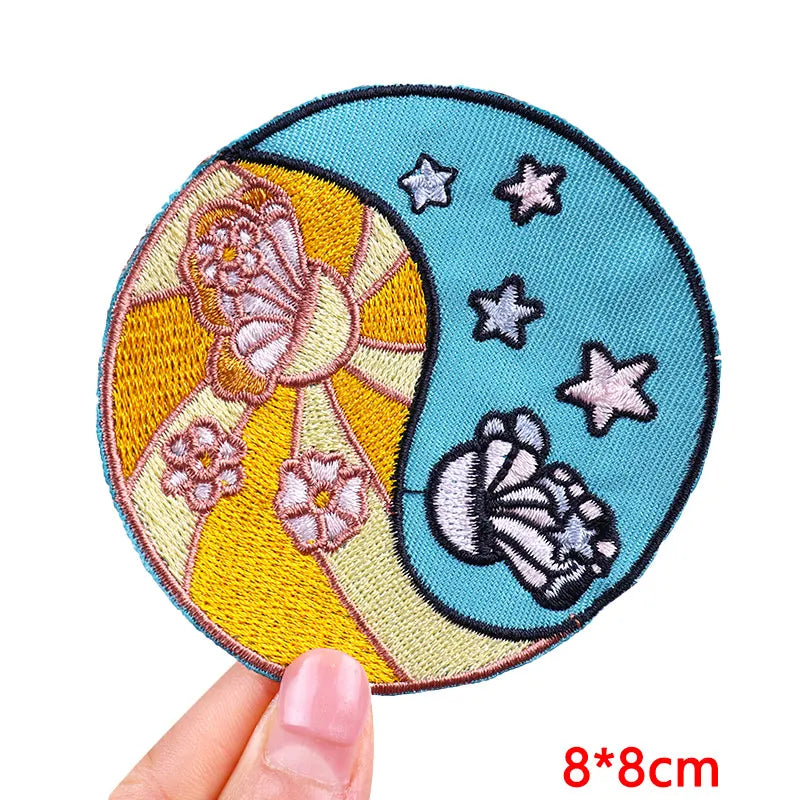 Circular embroidered patch with floral design held by a hand, on a white background.