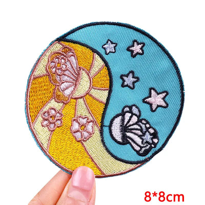 Circular embroidered patch with floral design held by a hand, on a white background.