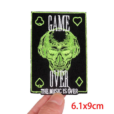 Embroidered patch with skull design and text 'GAME OVER THE MUSIC IS OVER' held by a hand.