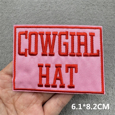 Pink patch with red text 'COWGIAL HAT' held in a hand against a gray background