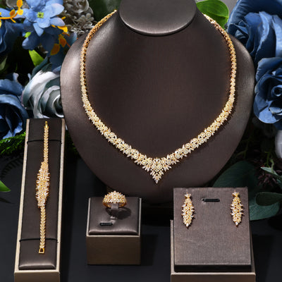 Gold bridal jewelry set including necklace, bracelet, ring, and earrings on a dark brown stand with floral background.
