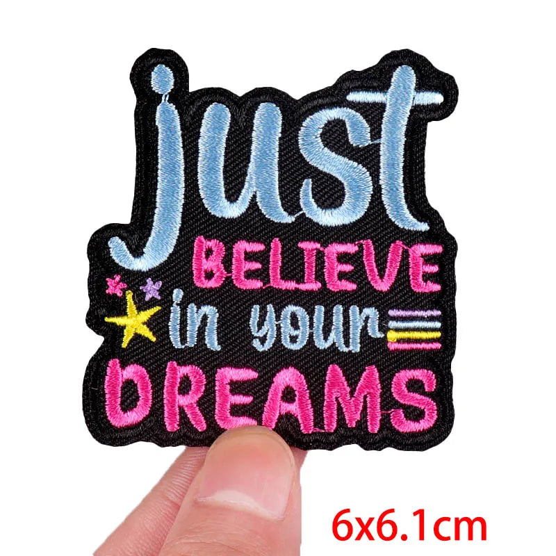 Motivational patch with 'Just Believe in Your Dreams' text held by a finger on a white background