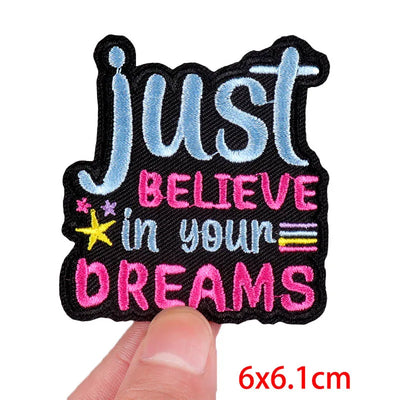 Motivational patch with 'Just Believe in Your Dreams' text held by a finger on a white background