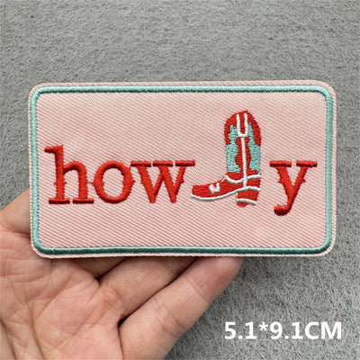 Embroidered patch with 'howdy' text and a boot design held by a hand on a gray background.