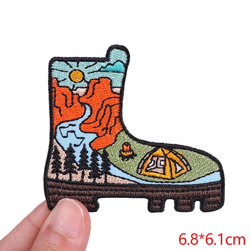 Embroidered patch of a boot with nature-themed design held by a hand, on a white background.