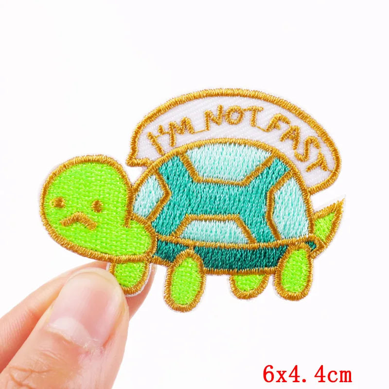Embroidered patch of a turtle with 'I'm Not Fast' text held by a hand on a white background.