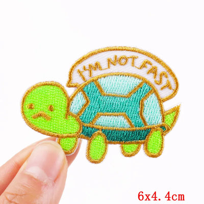Embroidered patch of a turtle with 'I'm Not Fast' text held by a hand on a white background.