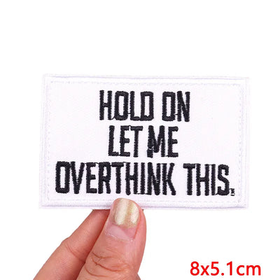 Embroidered patch with 'Hold on let me overthink this' text held by a hand.
