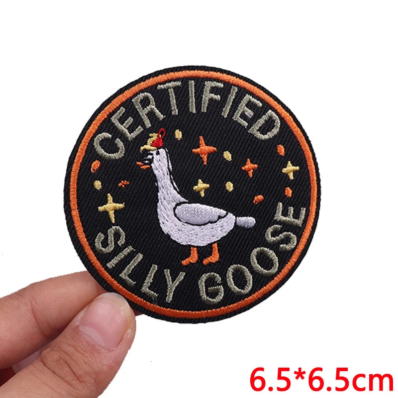 Round patch with a goose illustration and text 'Certified Silly Goose' held by a hand on a white background.