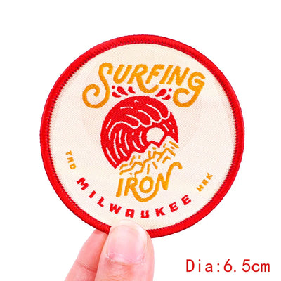 Circular patch with 'Surfing Iron Milwaukee' design held by a hand, on a white background.