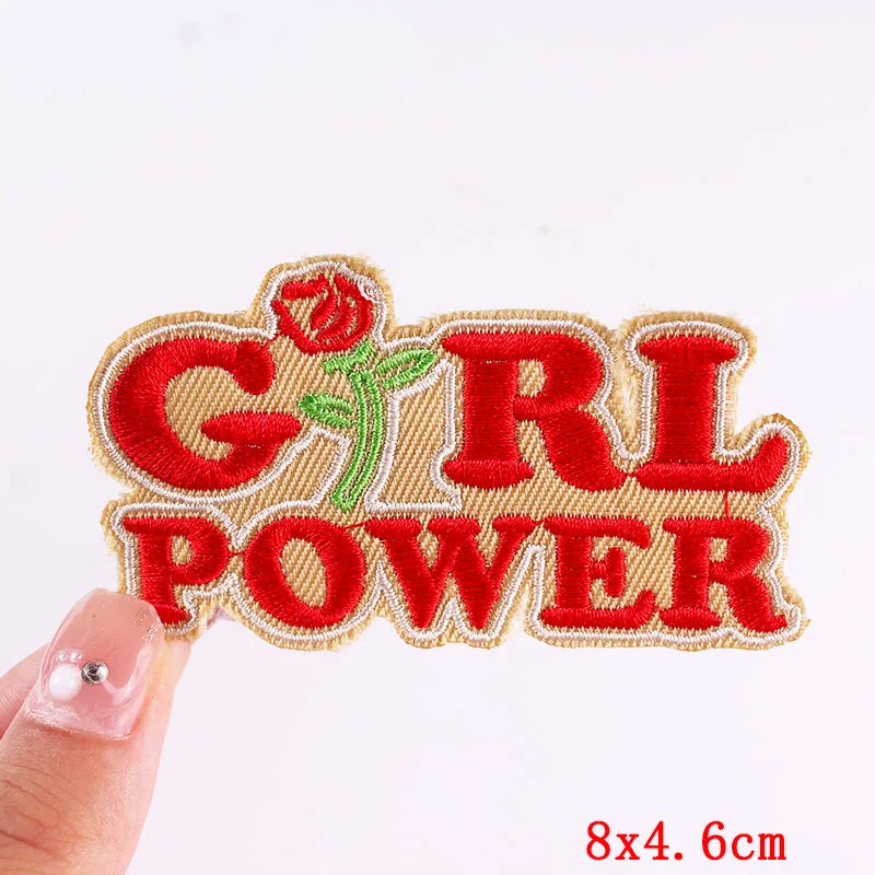 Embroidered patch with 'GIRL POWER' text and a rose, held by a hand against a white background.