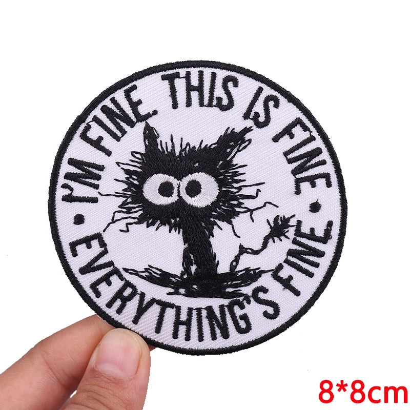 Circular patch with a black cat illustration and text held by a hand on a white background
