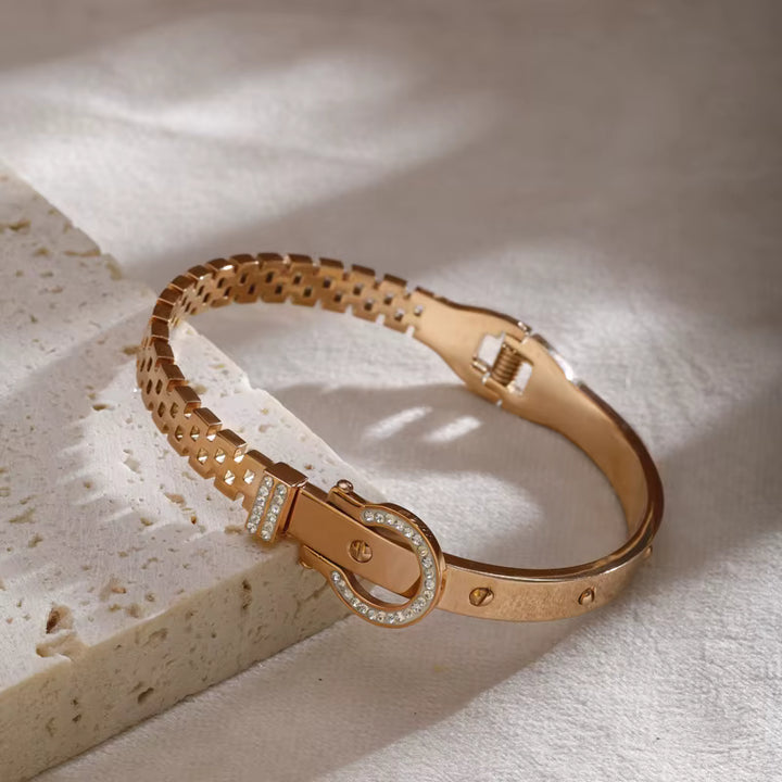 Rose gold bracelet with diamond accents on a textured beige surface