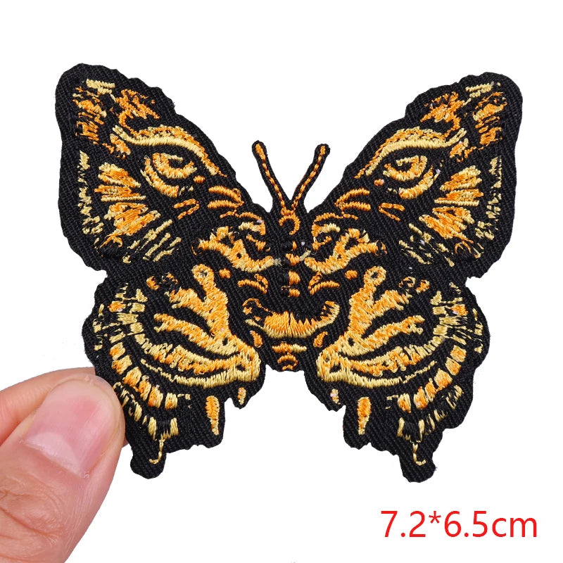 Butterfly patch with gold and black design held by a hand, on a white background.