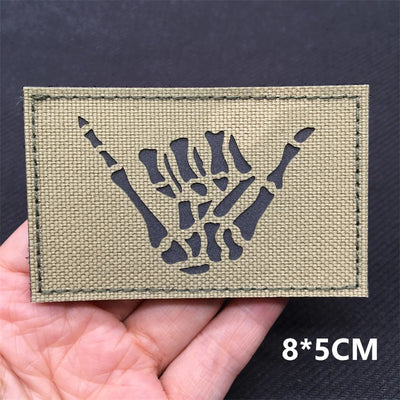 Kaki green patch with black skeleton hand design held in a hand against a dark background