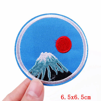 Circular patch with Mount Fuji and a red sun on a blue background, held by a hand.