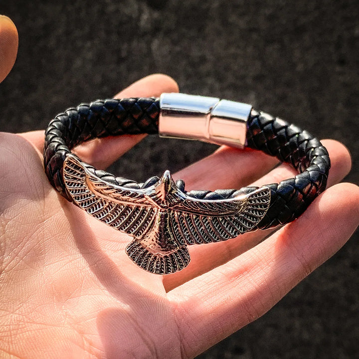 Black braided bracelet with an eagle clasp held in a hand against a dark background