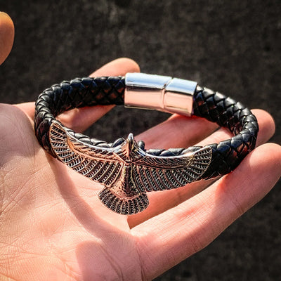 Black braided bracelet with an eagle clasp held in a hand against a dark background
