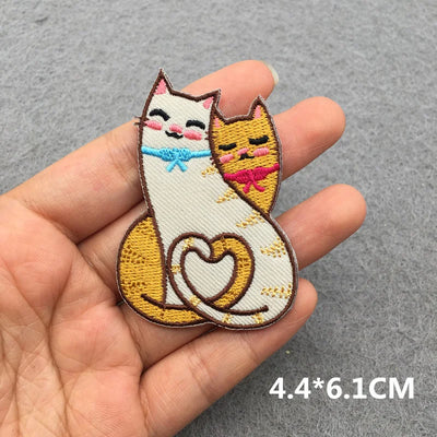 Embroidered patch of two cats sitting together with a heart on a gray background
