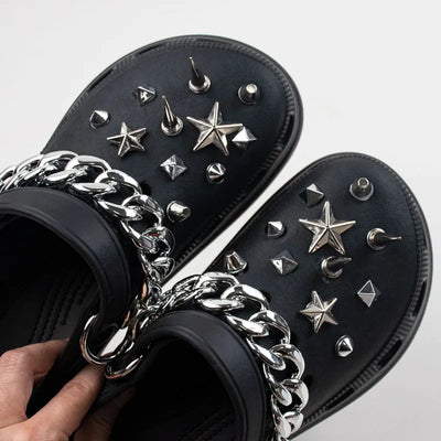 Black sandals with silver Rivet Shoe Charms and chains on a light gray background