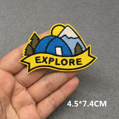 Embroidered patch with 'EXPLORE' text and camping design held in a hand on a gray background.