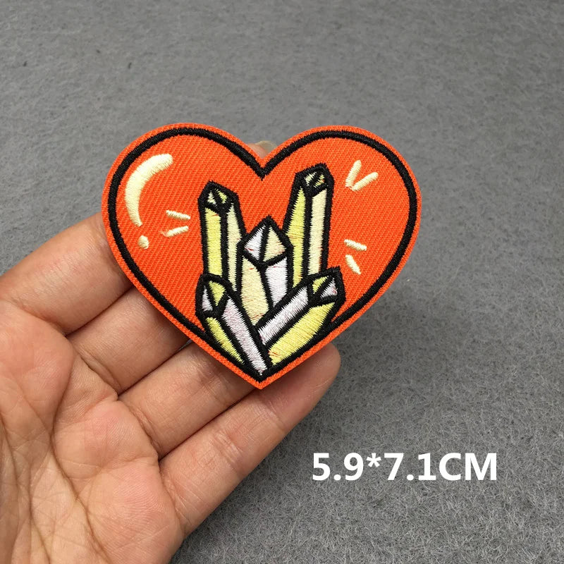 Heart-shaped patch with crystals held in a hand on a gray background