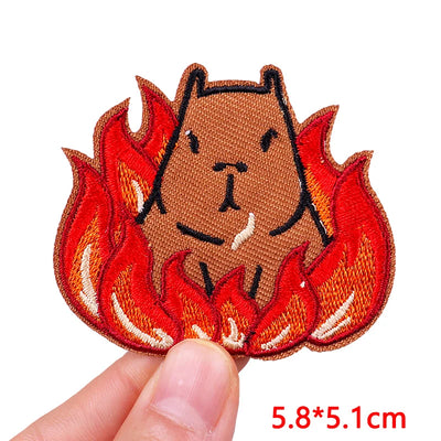 Embroidered patch of a bear surrounded by flames held by a hand on a white background.