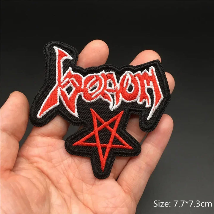 Hand holding a black red and white Venom embroidered iron-on patch with pentagram design 7.7x7.3cm on a dark background