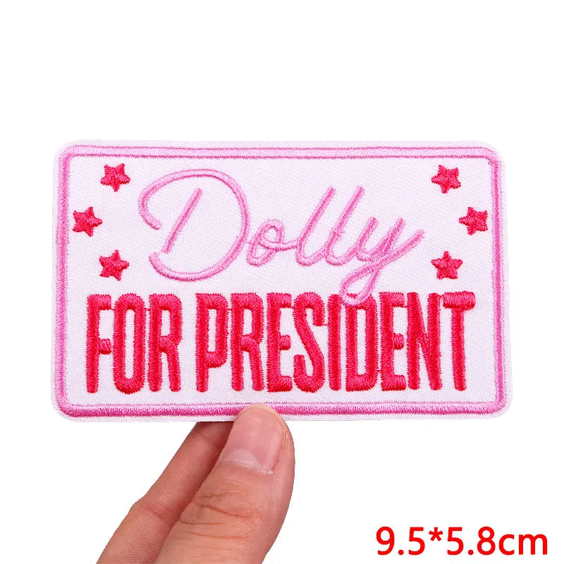 Embroidered patch with 'Dolly for President' text held by a hand on a white background