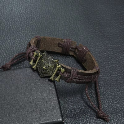 Brown leather bracelet with a metal wolf pendant on a textured gray surface