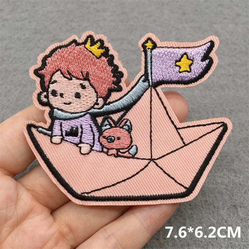 Embroidered patch of a character with pink hair and a small creature on a paper boat, held by a hand.