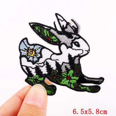 Embroidered patch of a donkey with flowers held by a hand, on a white background.