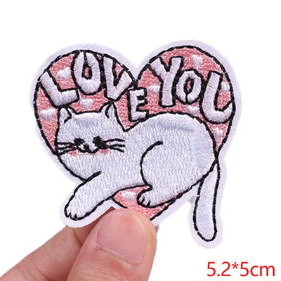 Heart-shaped patch with a cat and 'I love you' text held by a hand on a white background