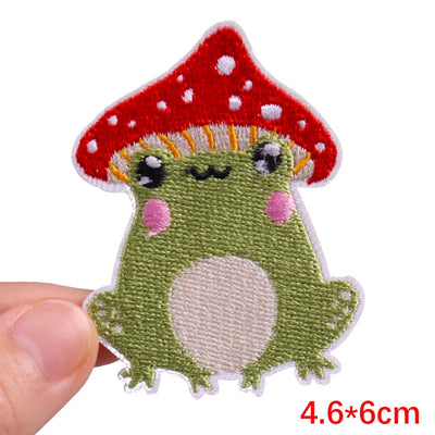 Embroidered patch of a green creature with a red mushroom on a white background