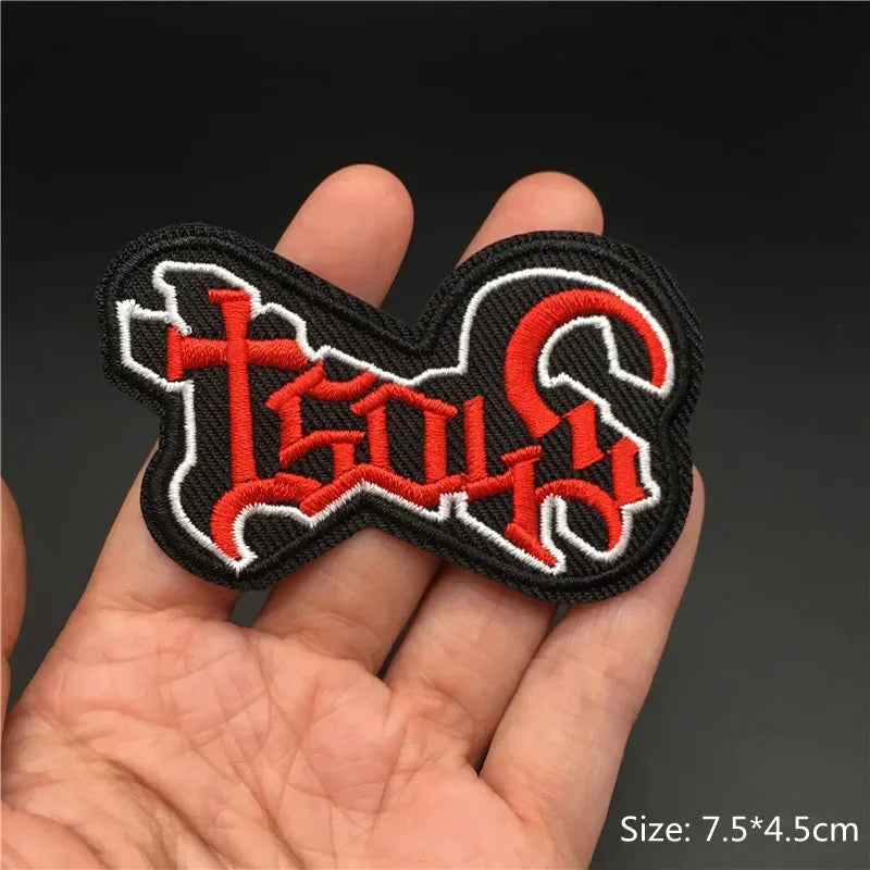 Embroidered patch with red and white design held in a hand against a dark background